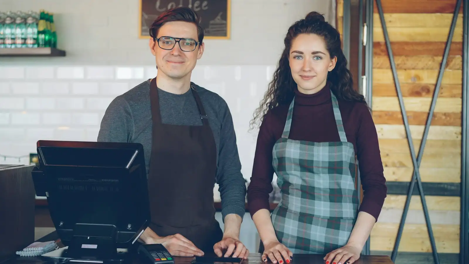 Two café owners in aprons standing at their counter
