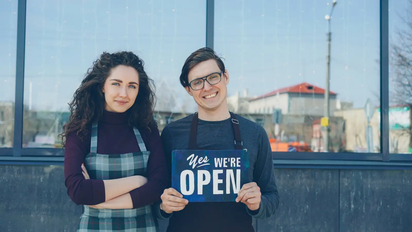 Two owners holding a 'Yes, we're open' sign outside their business